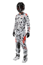 Alpinestars 2024 Techstar Rantera Pants, calças de motocross, camuflado cinzento Haze Gray, usadas com camisola a condizer, capacete preto e botas brancas e pretas, com padrões abstratos pretos e detalhes vermelhos, equipamento completo de corrida todo-o-terreno