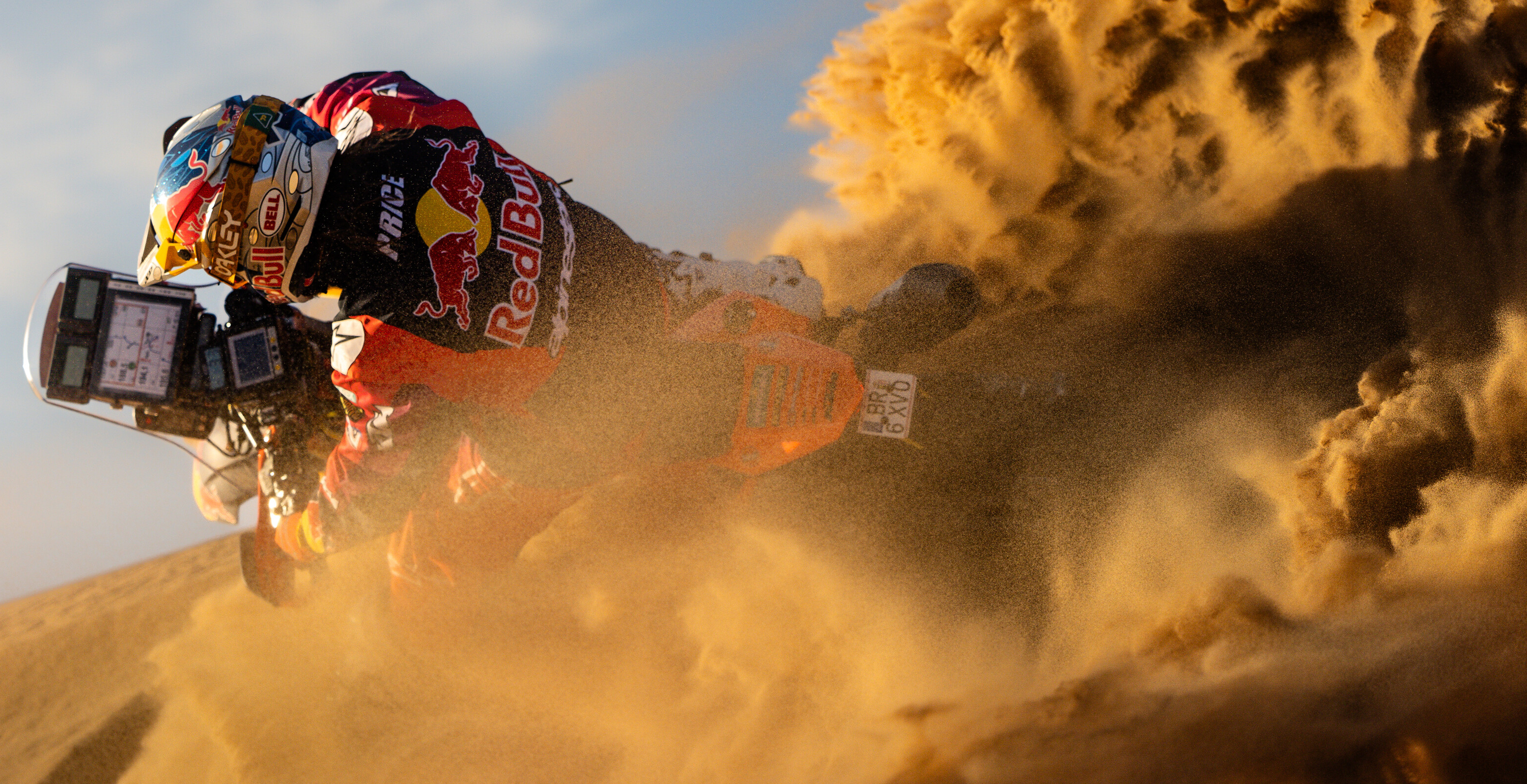 Toby Price riding a dirt bike through sand with a Red Bull branded helmet and Alpinestars enduro gear.