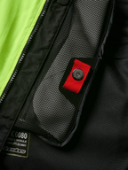 Alpinestars Tech-Air® 3 V2 System detail, close-up of internal mesh pocket with red pull tab and snap fastener, vibrant yellow fluo panel, black textile construction showing airbag module label and zipper