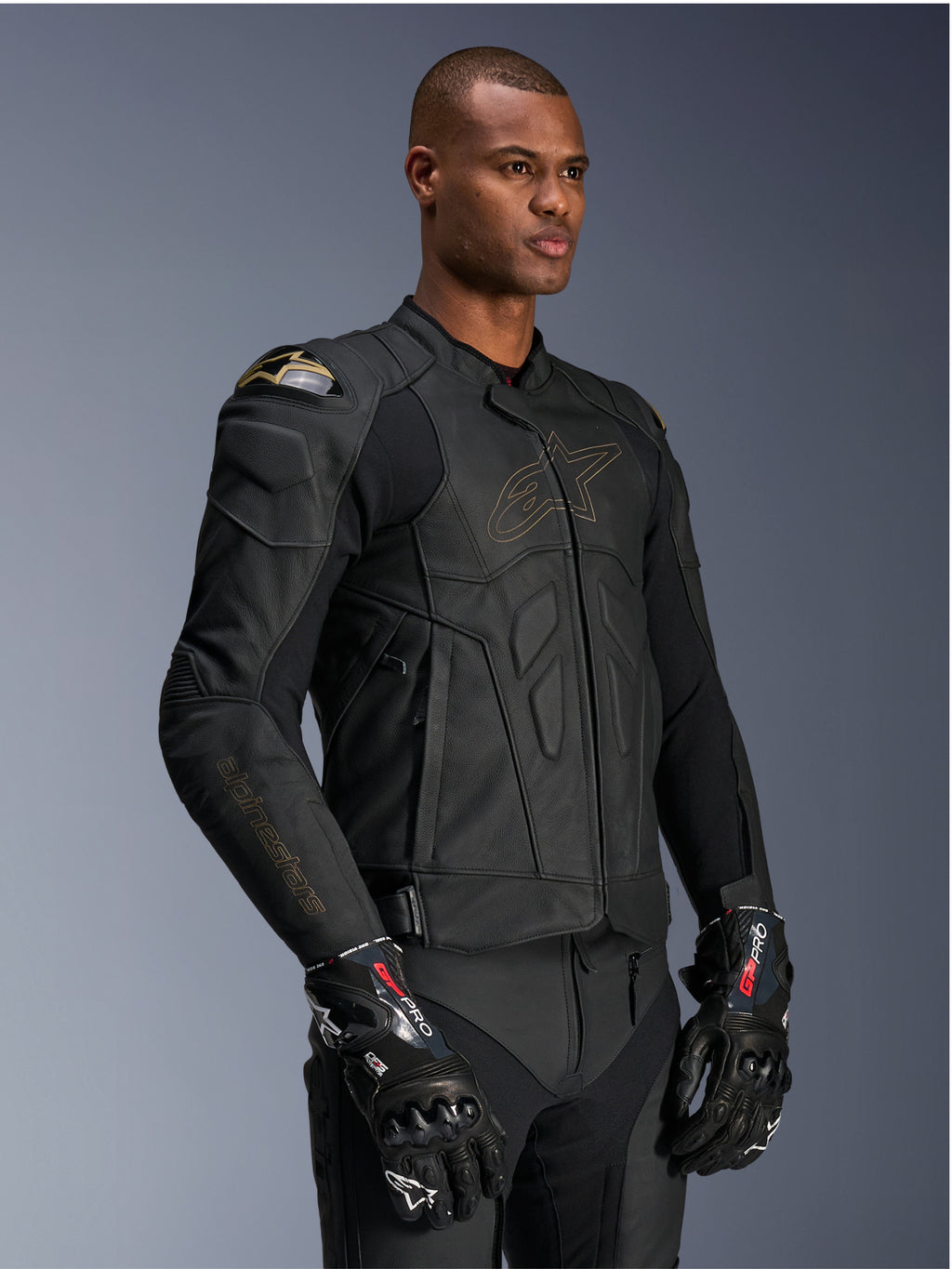 Alpinestars Dusk Leather Jacket, Black Laser motorcycle jacket, premium leather construction with gold Alpinestars logo outline and sleeve branding, external DFS shoulder protection, paired with GP Pro gloves, performance racing gear
