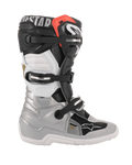 Botas Alpinestars Tech 7S Jovem, botas de motocross, preto, prateado, branco e dourado, vista de perfil lateral com estrutura inferior prateada, painéis superiores pretos e brancos, detalhe vermelho no topo do cano e sistema de fecho com três fivelas