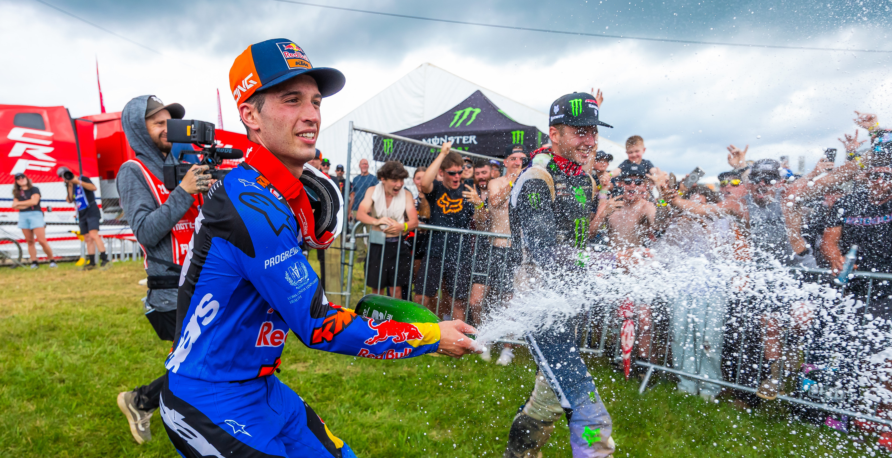 Tom Vialle celebrating with champagne on a grassy track, surrounded by spectators and event branding.