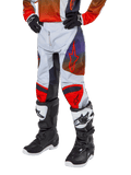Alpinestars 2024 Youth Racer Hoen Pants, calças de motocross para jovens, cinzento claro com detalhes em laranja vibrante e preto, com logótipos de estrela vermelha nas coxas e painéis vermelhos nos joelhos, usadas com botas pretas e brancas, design durável para todo-o-terreno