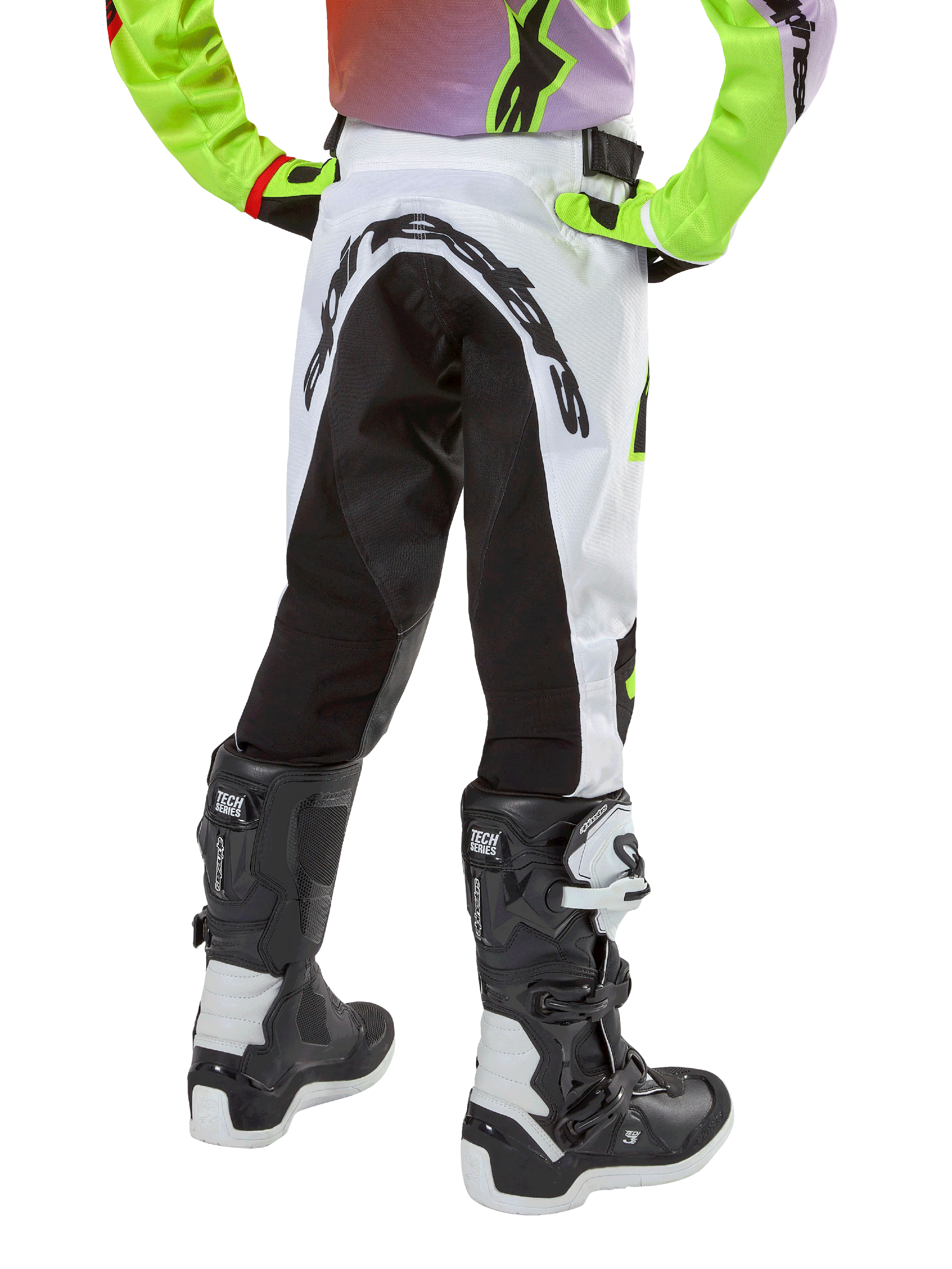 Alpinestars Youth 2024 Racer Lucent Pants, calças de motocross para jovens, brancas e pretas com detalhes néon, vista traseira mostrando o grande painel elástico traseiro e o logótipo Alpinestars, usadas com botas Alpinestars Tech Series pretas e brancas.