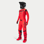 Motocross rider wearing complete racing gear, Supertech Ember LE Jersey and Pants in Red Fluo and Black, black helmet with goggles, matching red and black boots and gloves, coordinated professional outfit for off-road racing
