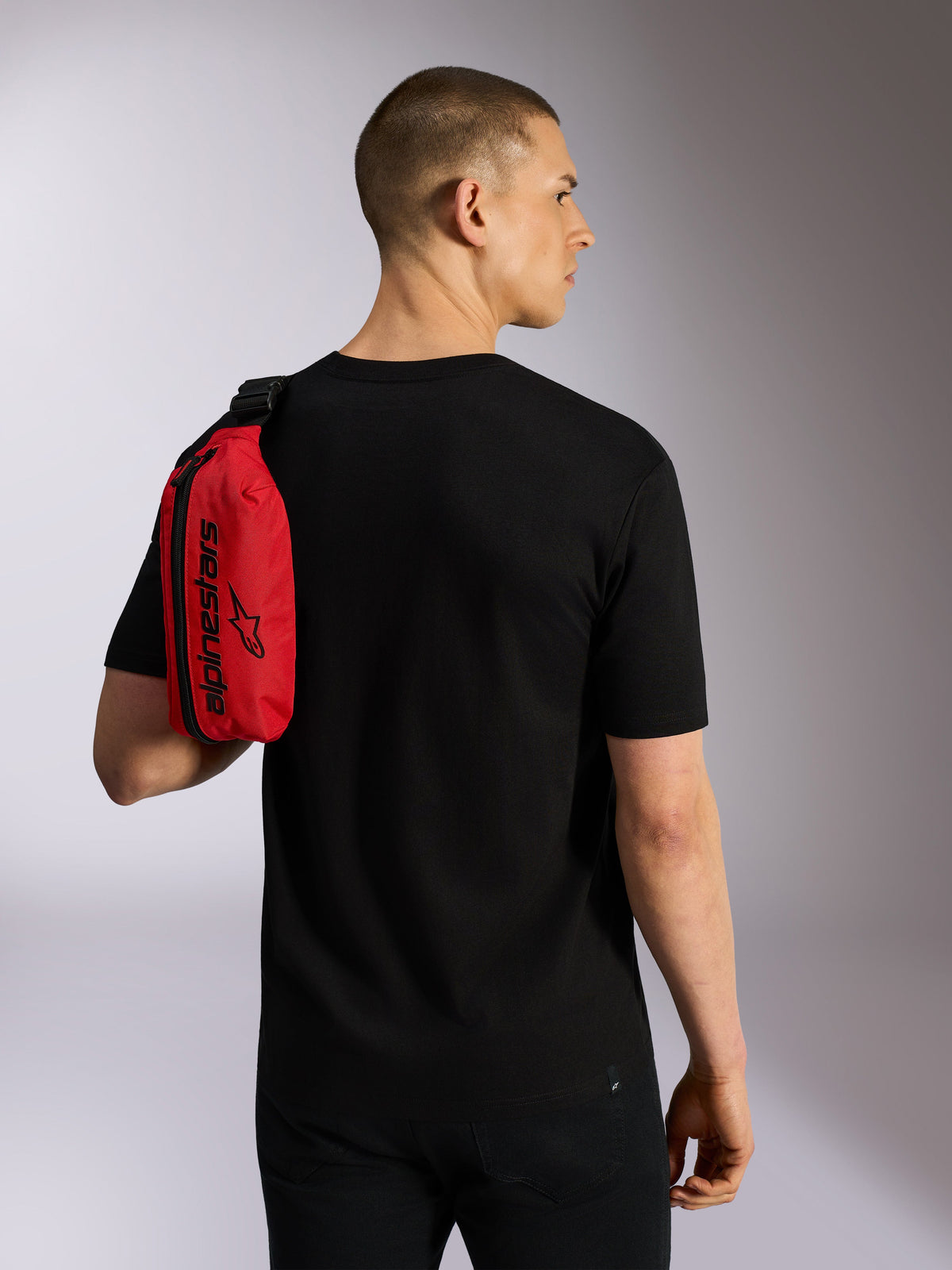Alpinestars Only Linear Hip Bag, vermelha e preta, usada sobre o ombro como uma bolsa tiracolo por um modelo com t-shirt preta, com fecho de correr vertical e logótipo Alpinestars preto, acessório urbano resistente.